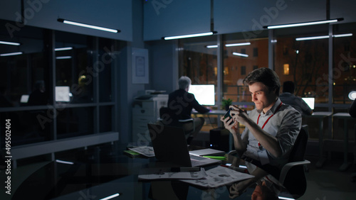 Young businessman play video game on cellphone working late in office