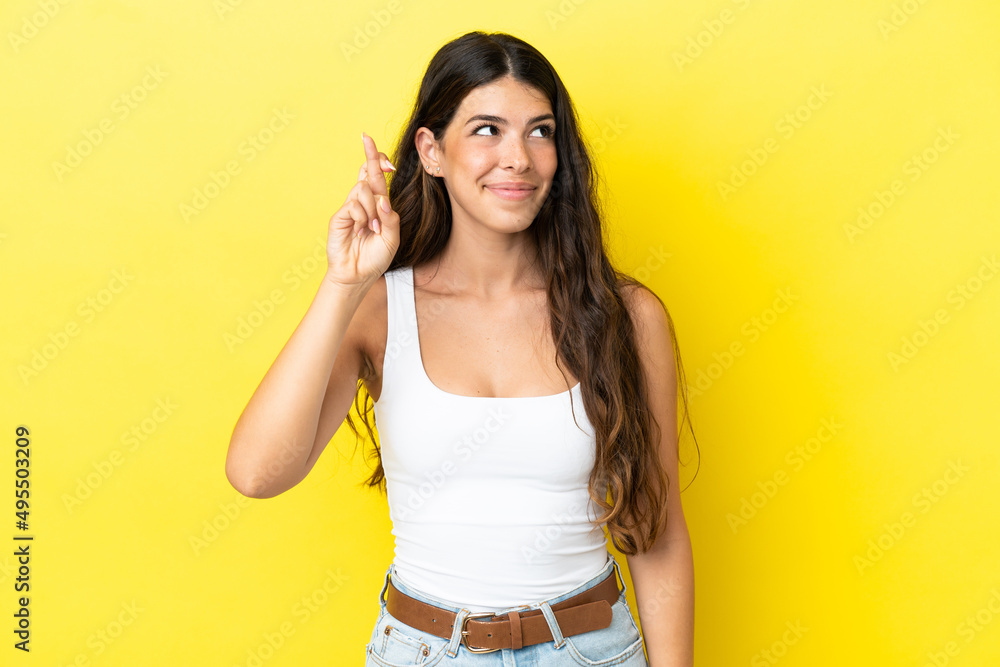 Young caucasian woman isolated on yellow background with fingers crossing and wishing the best Young caucasian woman isolated on yellow background with fingers crossing and wishing the best