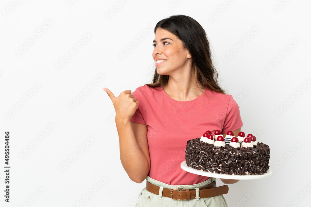 Young caucasian woman holding birthday cake isolated on white background pointing to the side to present a product Young caucasian woman holding birthday cake isolated on white background pointing to the side to present a product