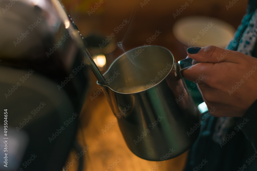 Unrecognizable woman's hand preparing textured milk on a professional espresso machine. Making a cappucino in a rustic coffee shop.