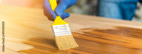 A man covers an oak table with oil with a yellow brush in blue rubber gloves. oiled wooden table top.