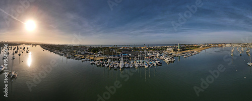 panorama of boats docked at Newport Beach CA during sunrise over calm harbor waters and the ocean with clouds in the sky