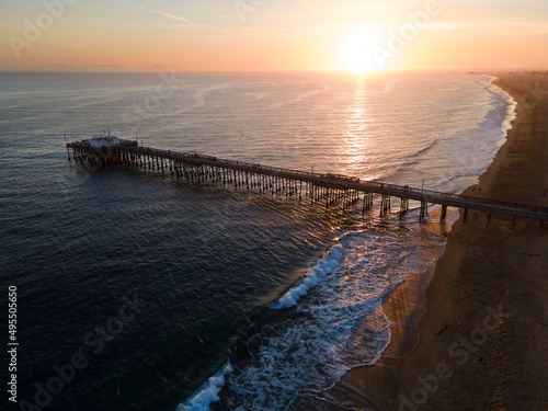 sunset at Newport Beach pier with ocean waves and sandy beach aerial view