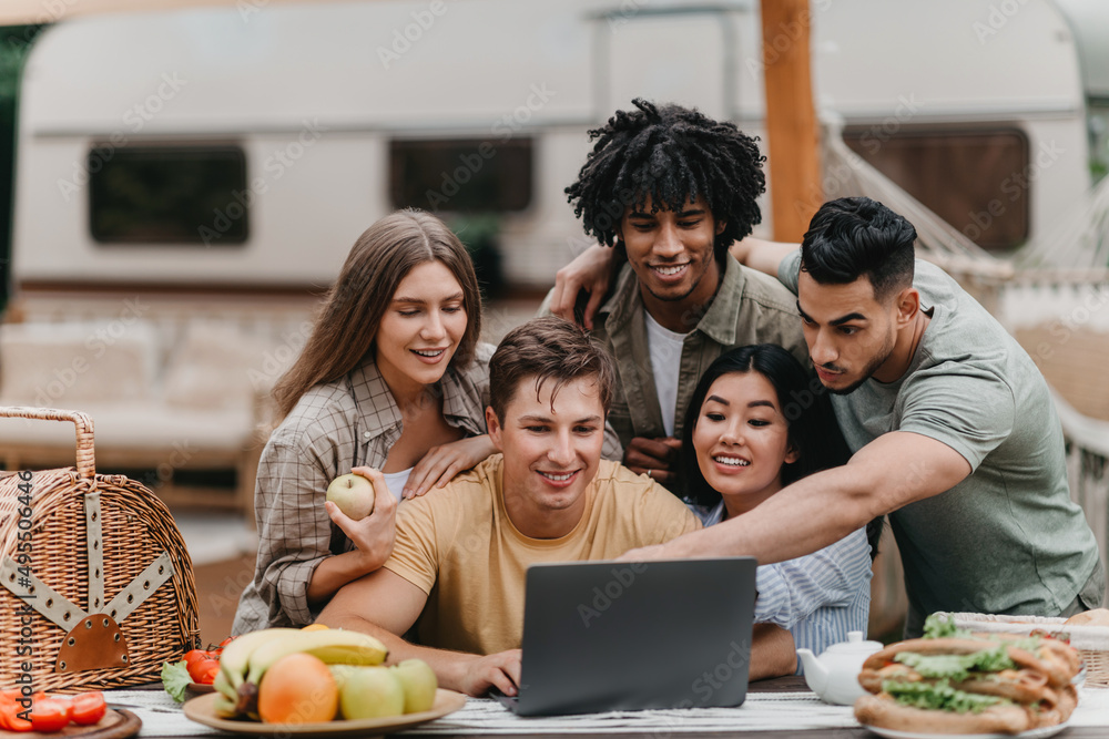 Group of interracial young people using laptop while camping in countryside, video chatting online, having fun Group of interracial young people using laptop while camping in countryside, video chatting online, having fun