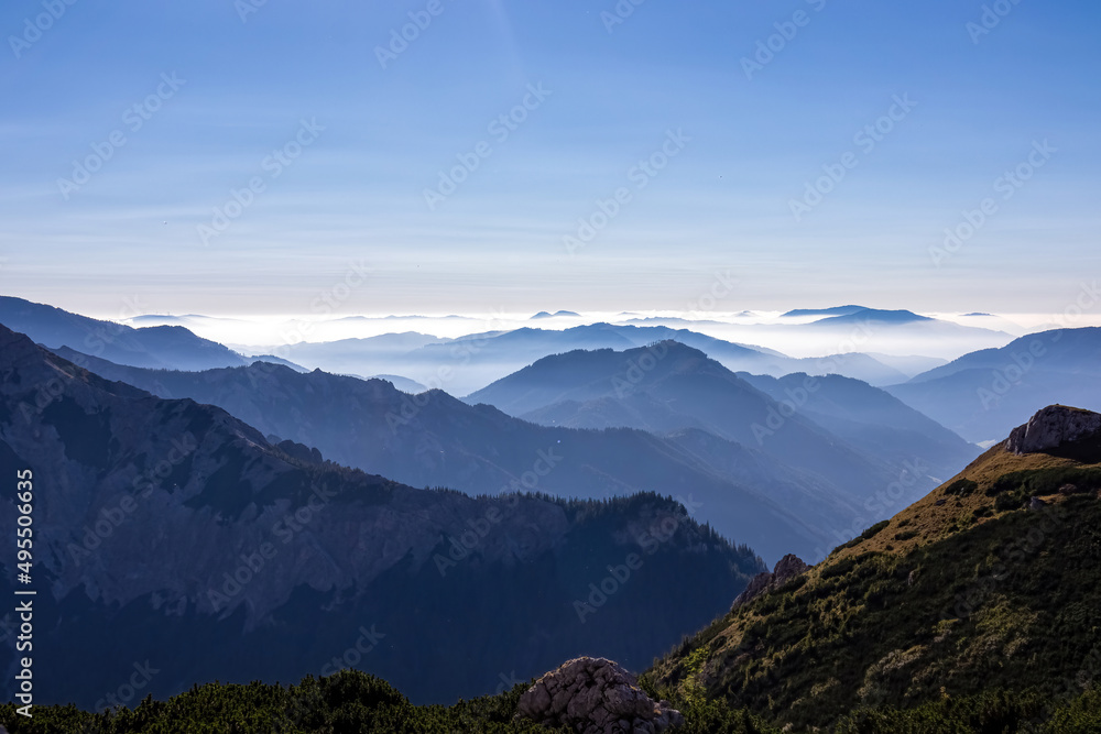 Obraz premium A panoramic view on the mountain peaks of the Hochschwab Region in Upper Styria, Austria. Cloudless weather on a sunny summer day in the Alps. Blue misty valley and soft hills. Concept freedom