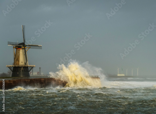 Netherlands, Vlissingen, Waves crashing against pier with windmill photo