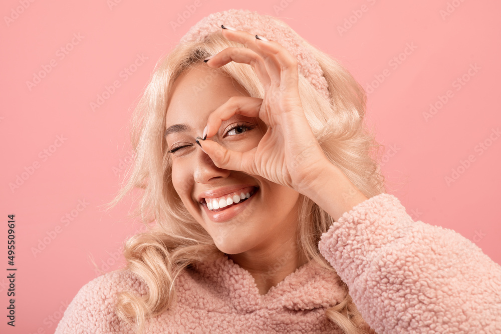 Happy young woman having fun on pink studio background, making eyewear with her fingers and smiling at camera