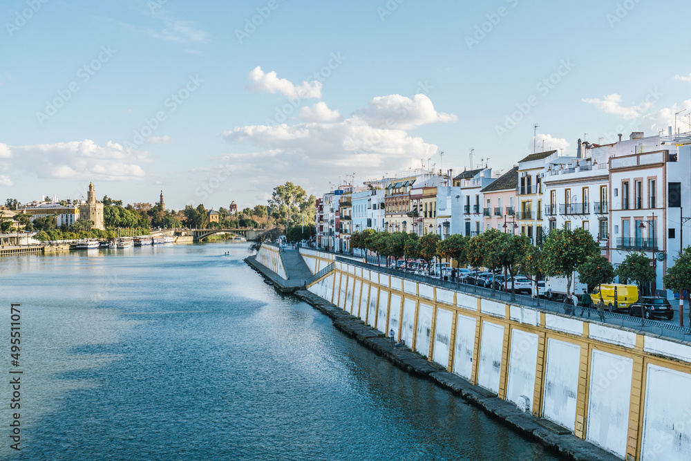 View of the buildings of Triana District next to the river, the San Telmo Bridge and the Golden Tower in Seville, Spain.