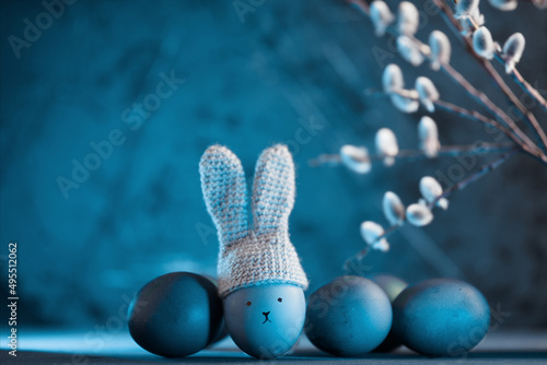 Easter eggs on a blue background copy space . Crocheted hat with bunny ears. Willow branch.