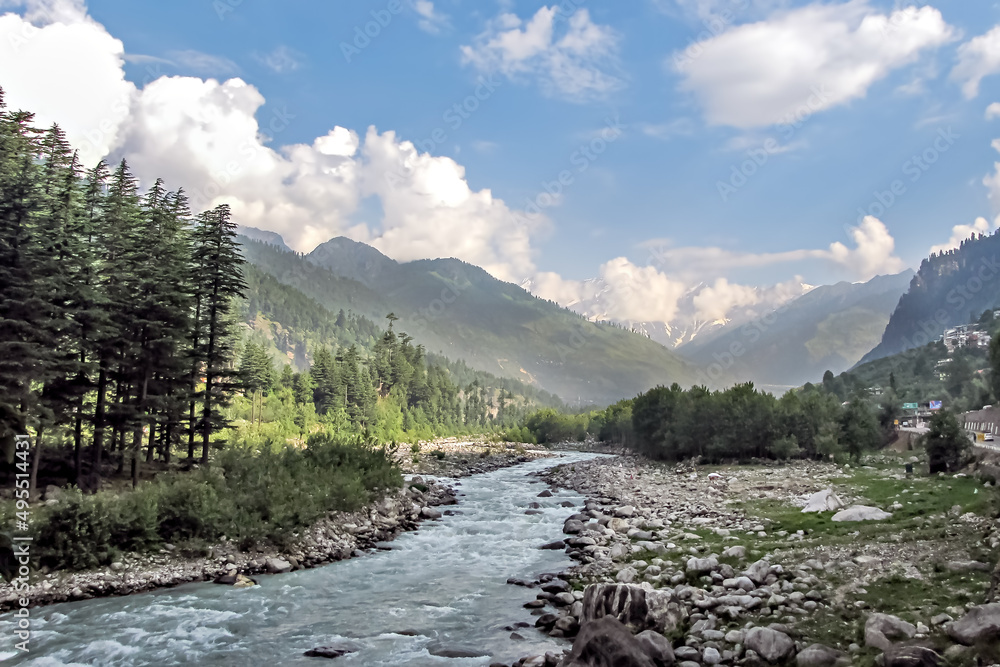 Beas river with snow cladded mountain , blue clouds and greenery in the background.