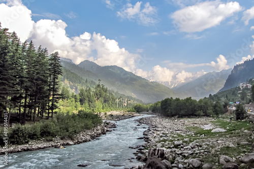 Beas river with snow cladded mountain , blue clouds and greenery in the background. photo
