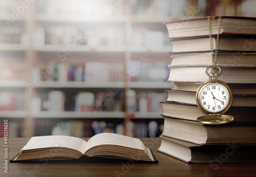 Old clock on a chain with stack books on library background. Retro clock as a symbol of time a books.