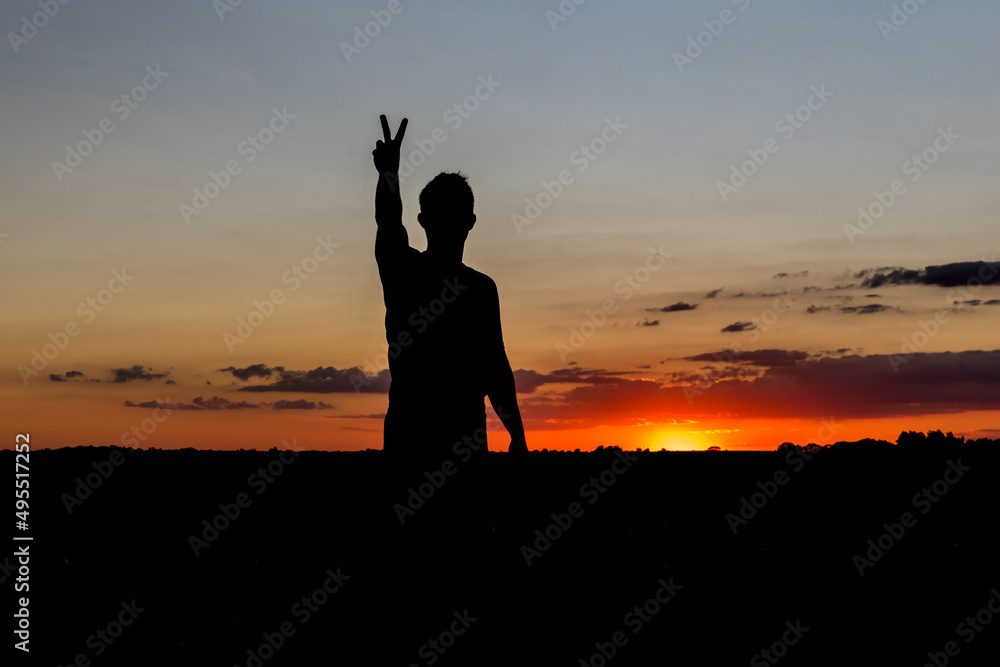 Sunset silhouette with boy showing hand with peace and love symbol.