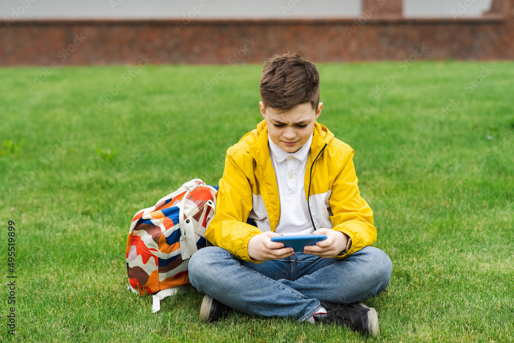 Boy playing on a smartphone sitting on a green lawn after school