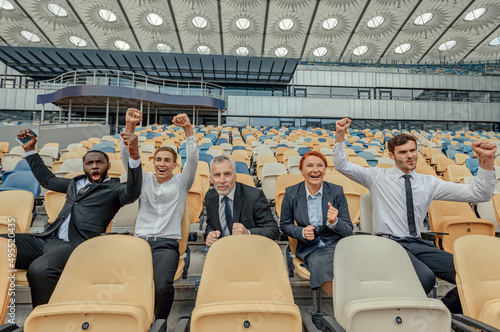Excited people in business suits sitting in fan zone of stadium