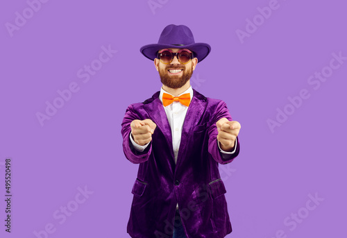 Tableau sur toile Portrait of excited male entertainer in velvet suit isolated on purple studio background point at screen