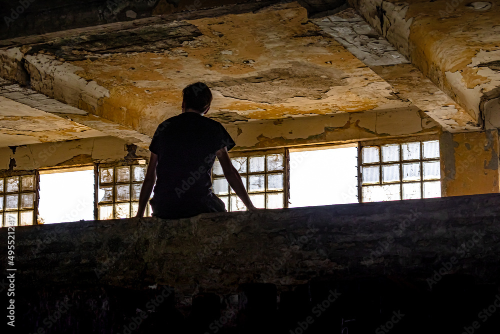 Silueta de hombre joven sentado mirando por la ventana en lugar abandonado Silueta de hombre joven sentado mirando por la ventana en lugar abandonado