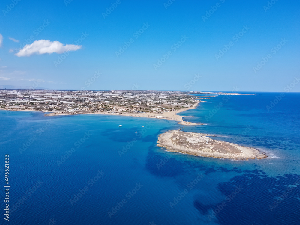 Aerial drone view of island and beach of Isola delle Correnti. Lighthouse surrounded by clear turquoise sea water in Portopalo di capo Passero, Sicily