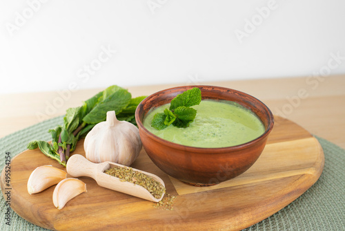Tasty green chutney sauce. With fresh mint pudina and yogurt. Spicy indian cuisine. Served on brown bowl with spices, garlic and parsley on wood board, light background. Healthy fresh dip