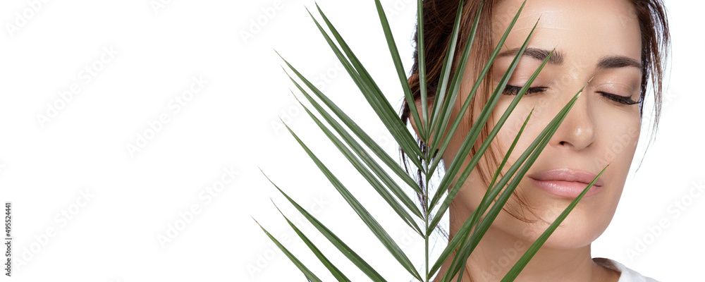 Beauty and Skincare Concept. Beautiful natural young woman face with nude makeup on a flawless skin with a palm leaf