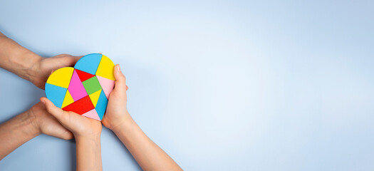 World autism awareness day concept. Adult and child hands holding puzzle heart on light blue background. Top view