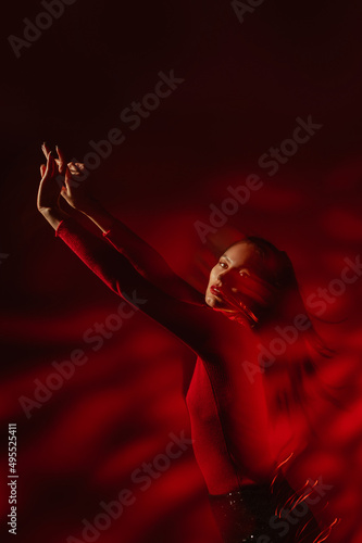 Fashion portrait with move effect and art lighting. Confident woman wearing red turtleneck, sequin trousers, posing in darkness 