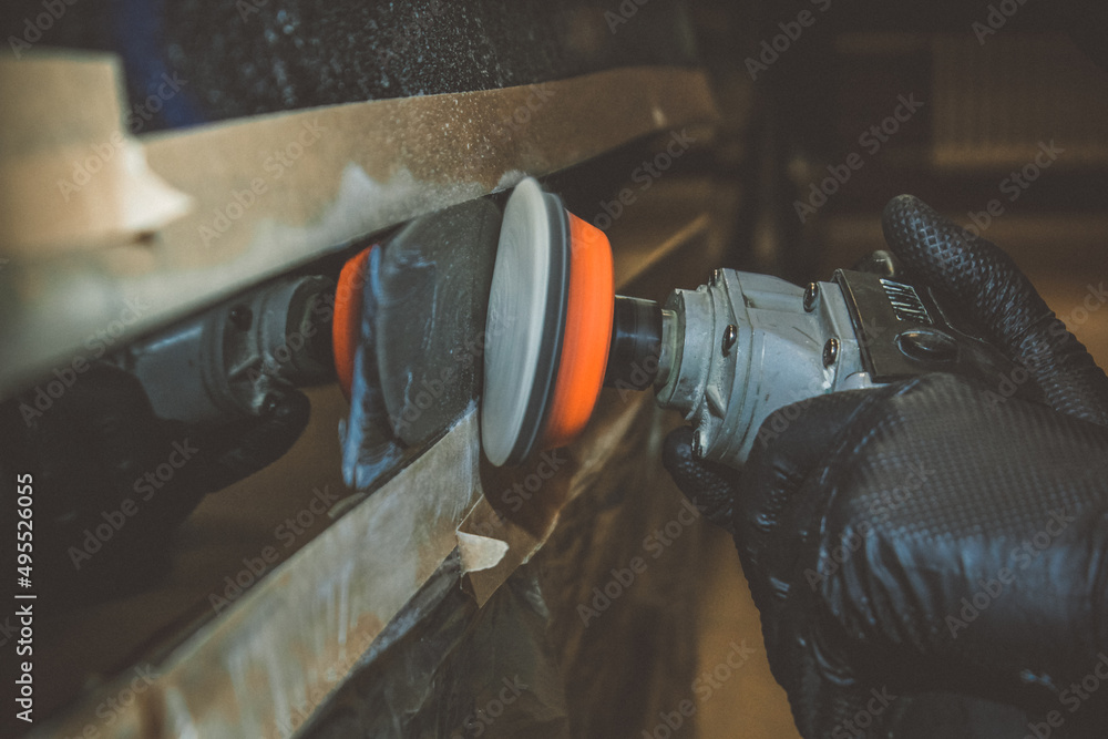 Car detailing - hands with an orbital polishing machine in an auto repair shop. Selective focus. A man polishes a car with a close-up grinder. Car detailing - hands with an orbital polishing machine in an auto repair shop. Selective focus. A man polishes a car with a close-up grinder.
