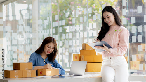 Two owners of an online store on the website are preparing parcels to send to customers following orders from the web page, they check the information and prepare for delivery to the customers. © kamiphotos