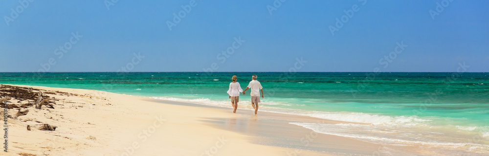 Panoramic view with loving seniors walking by ocean Panoramic view with loving seniors walking by ocean