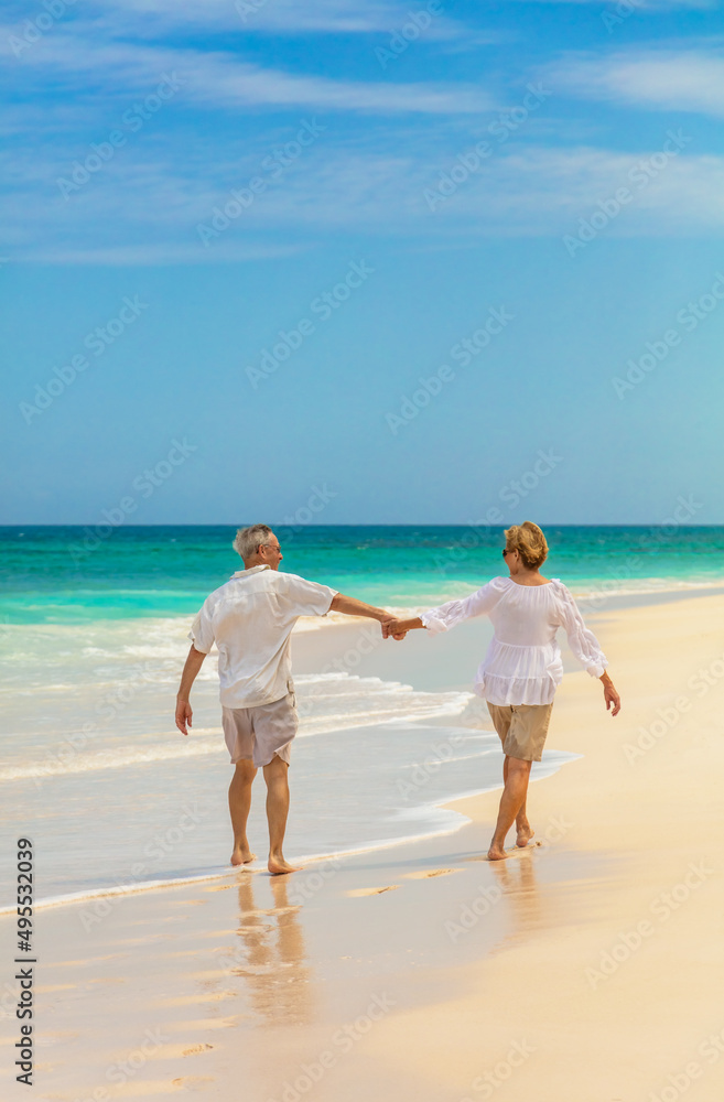 Mature couple holding hands walking along shoreline Bahamas