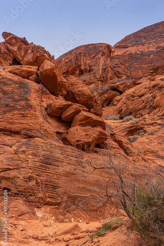 Overton, Nevada, USA - March 11, 2016: Valley of Fire. Portrait of red rock boulders partly covered with black shine in which pictographs have been edged. Blue sky and dry bush on desert floor.