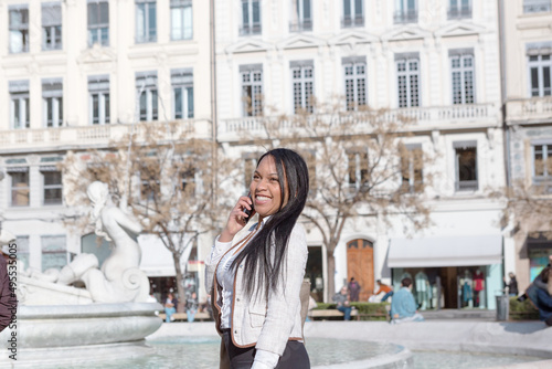 Young woman who stands with her smart phone in square of Jacobins with famous fountain in background in city of Lyon in France