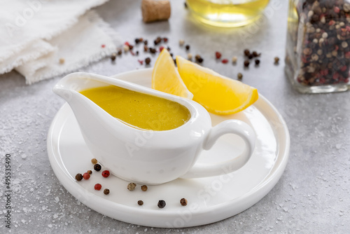 Vinaigrette sauce. Basic Vinaigrette or Citronette salad dressing with oil, lemon juice, salt and pepper served in white ceramic gravy boat. Closeup, ingredients on background. Horizontal. photo