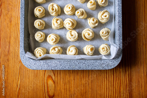 Baking dough in a baking tray. Dough for small buns. Home cooking baking cookies, buns in the form of roses, snails. The baking sheet is metallic gray. Wooden table. Top view.