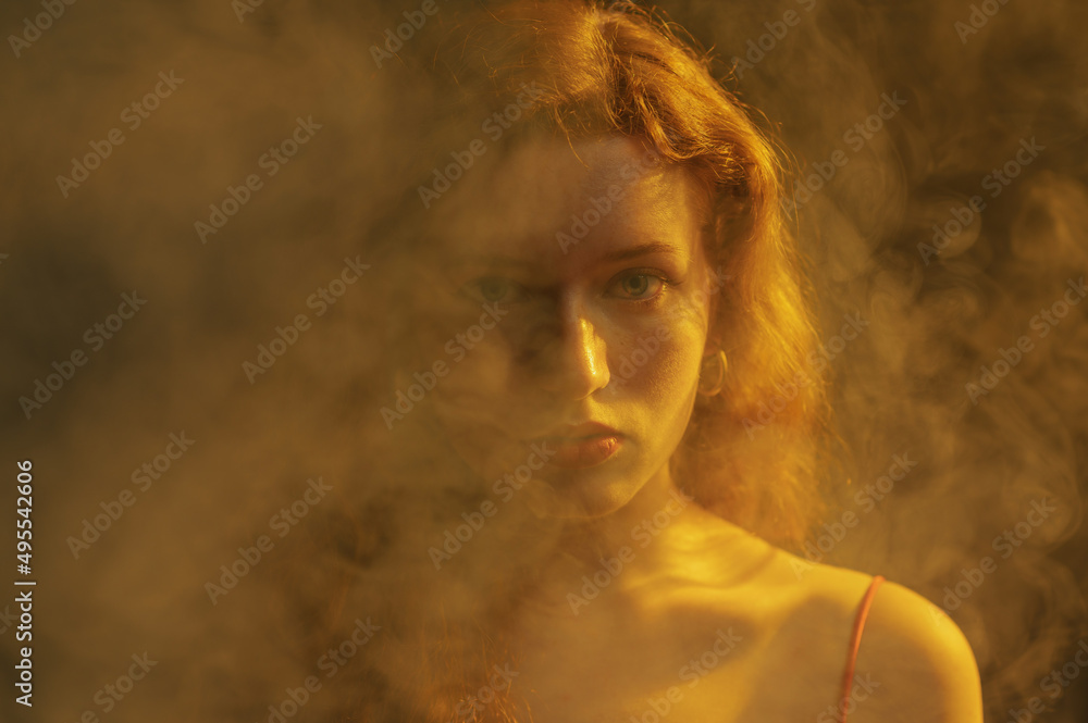 Close up studio art portrait of beautiful redhead freckled woman posing in smoke, darkness and warm light
