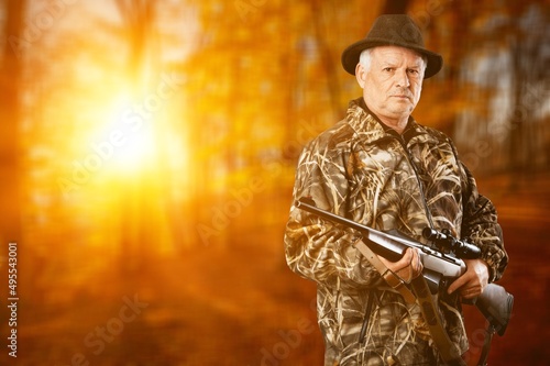 Male hunter in forest clothes holding gun ready to hunt, and walking in forest. Hunting and people concept.