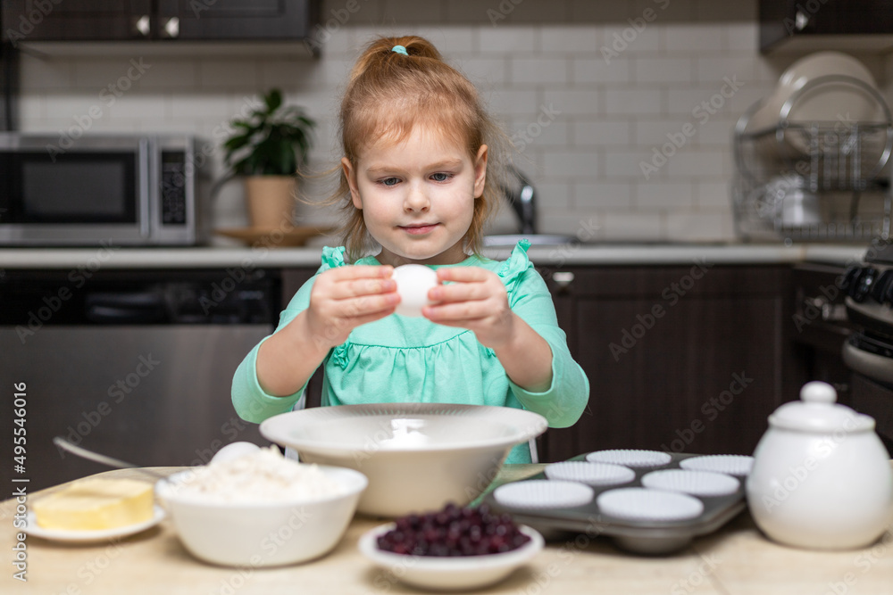 Little girl cooking muffins. Child in kitchen holding egg, ready to bake. Food on table Little girl cooking muffins. Child in kitchen holding egg, ready to bake. Food on table