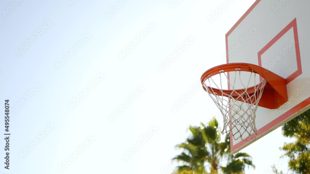 Orange hoop, net and backboard for basket ball game outside, basketball court outdoors. Recreational sport equipment on streetball field or playground. Blue sky and beach palm trees, California USA. Orange hoop, net and backboard for basket ball game outside, basketball court outdoors. Recreational sport equipment on streetball field or playground. Blue sky and beach palm trees, California USA.
