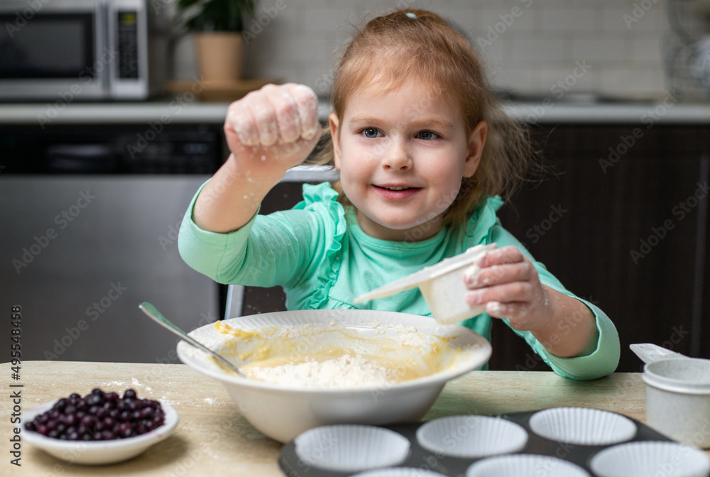 Small happy child cooking in kitchen. Little smiling girl making dough for muffins with berries. Small happy child cooking in kitchen. Little smiling girl making dough for muffins with berries.