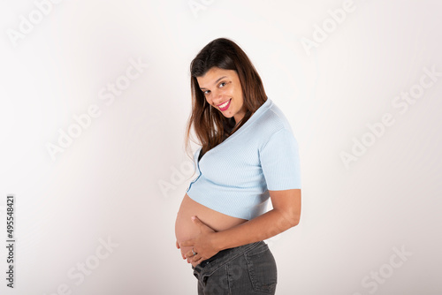 Portrait of a pregnant latin woman, touching her belly, with a relaxed and happy expression, on white background, copy space