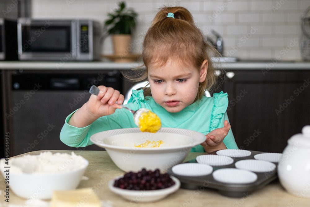 Little girl making dough in kitchen at home. Small child cooking food. Kid making homemade muffins Little girl making dough in kitchen at home. Small child cooking food. Kid making homemade muffins