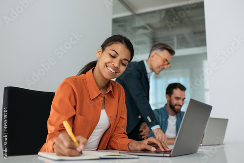 Group of diverse business people using laptop computers working together in office. Teamwork, meeting, successful business concept. African American manager taking notes planning start up at workplace