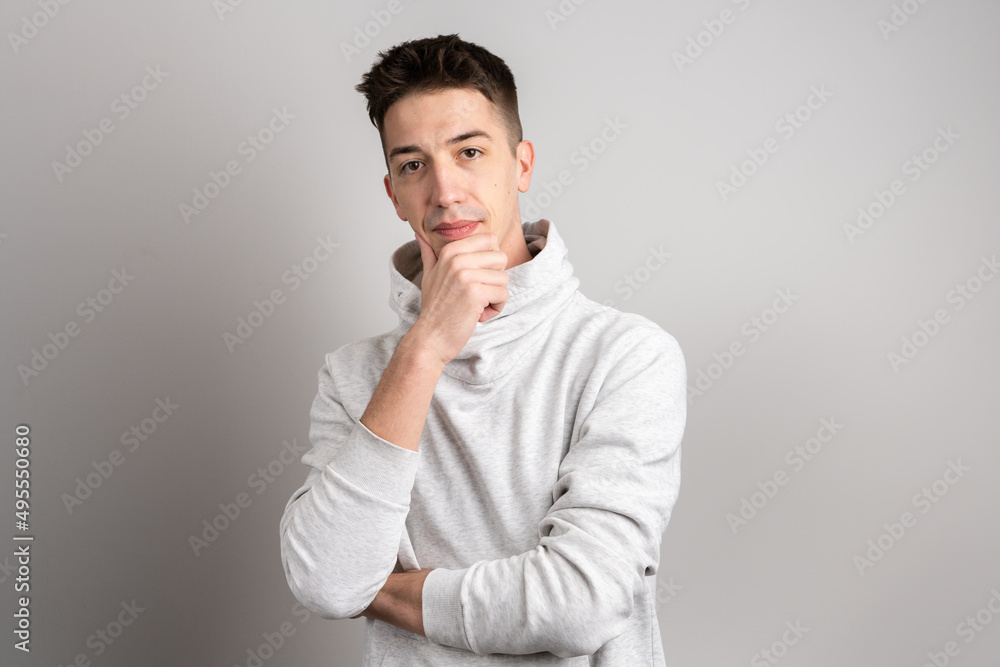 Portrait of one adult caucasian man 25 years old with short hair looking to the camera in front of white wall background thinking wearing light hoodie copy space Portrait of one adult caucasian man 25 years old with short hair looking to the camera in front of white wall background thinking wearing light hoodie copy space