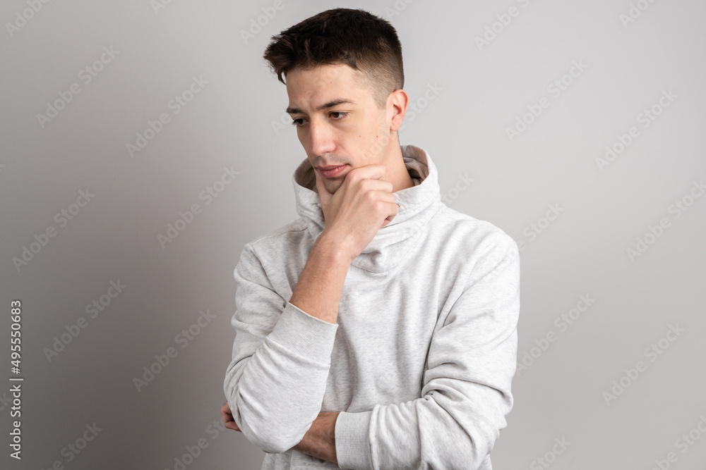 Portrait of one adult caucasian man 25 years old with short hair looking to the side in front of white wall background thinking wearing light hoodie copy space Portrait of one adult caucasian man 25 years old with short hair looking to the side in front of white wall background thinking wearing light hoodie copy space