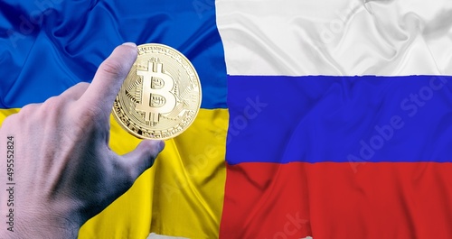 Hand holding a phisical gold  bitcoin coin symbol of cryptocurrency on the flag of Russia and Ukraine