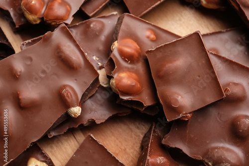 Pieces of tasty chocolate with nuts on board, closeup