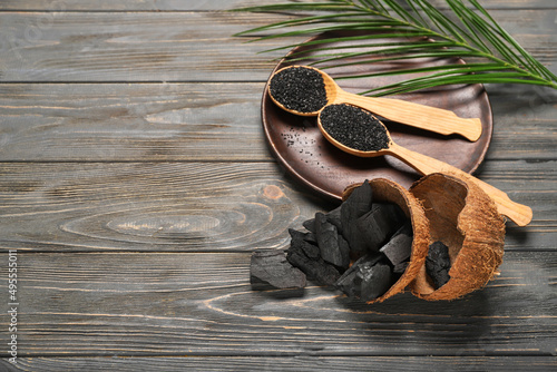 Coconut shells and spoons with activated carbon on dark wooden background photo