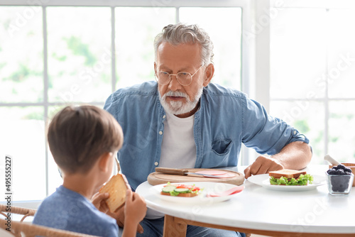 Senior man having breakfast with his grandson at table in kitchen