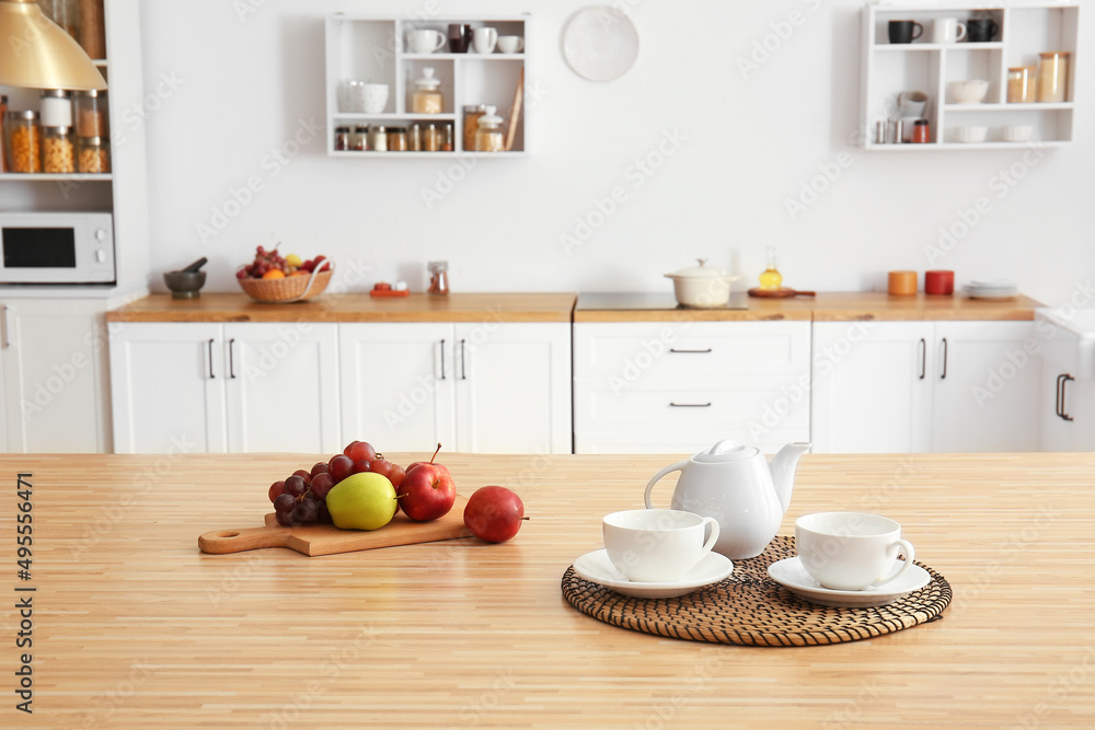 Teapot with cups, board and fruits on dining table in kitchen Teapot with cups, board and fruits on dining table in kitchen