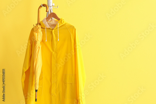 Rack with raincoat and umbrella near yellow wall